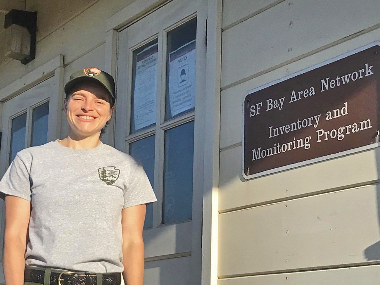 Botanist Lisa Schomaker is pictured smiling next to a sign for the San Francisco Bay Area Network Inventory & Monitoring Program.