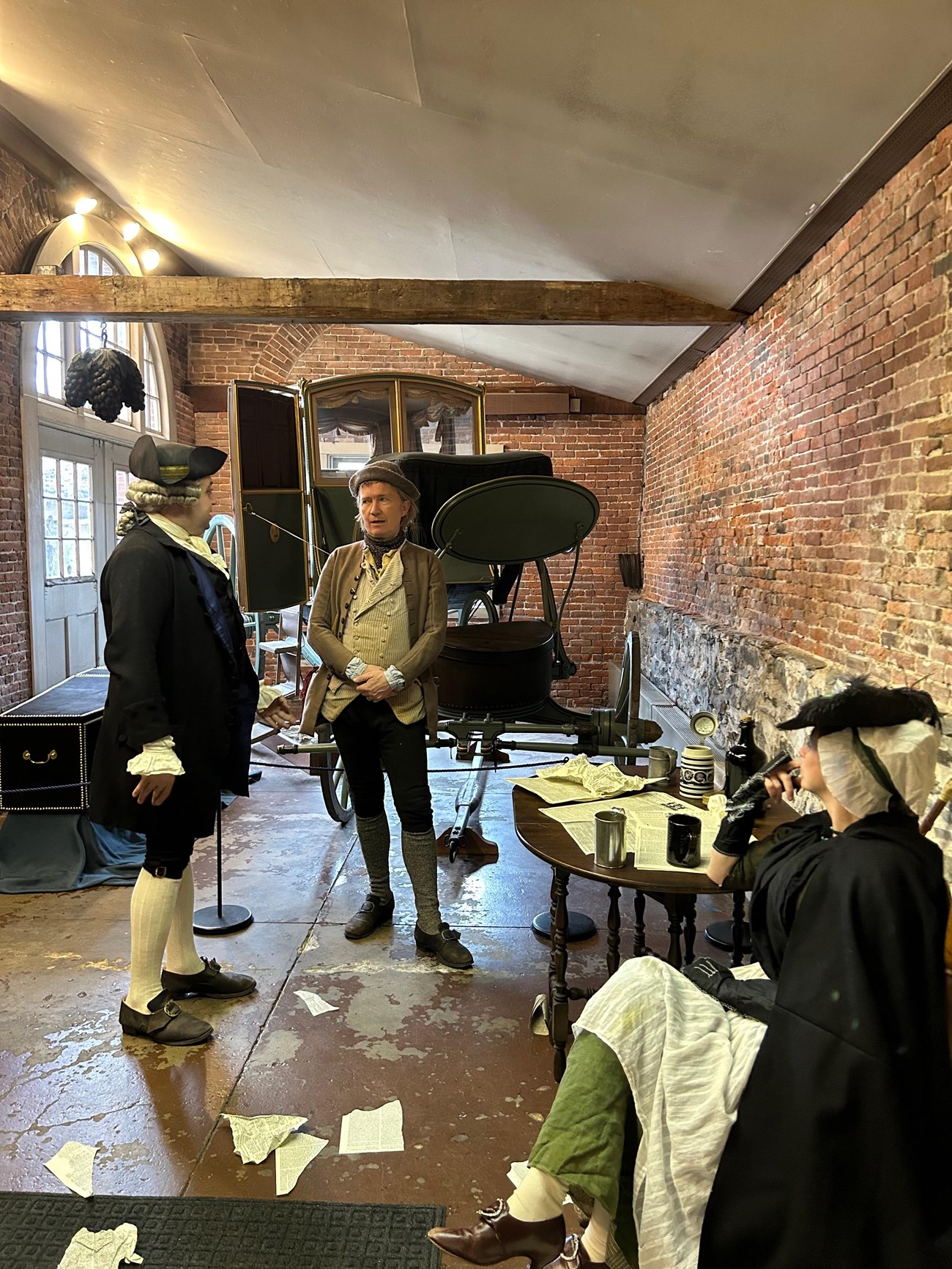 Living History JBH1 Two men standing in front of a carriage converse as seated woman listens. All individuals wearing colonial-era clothing
