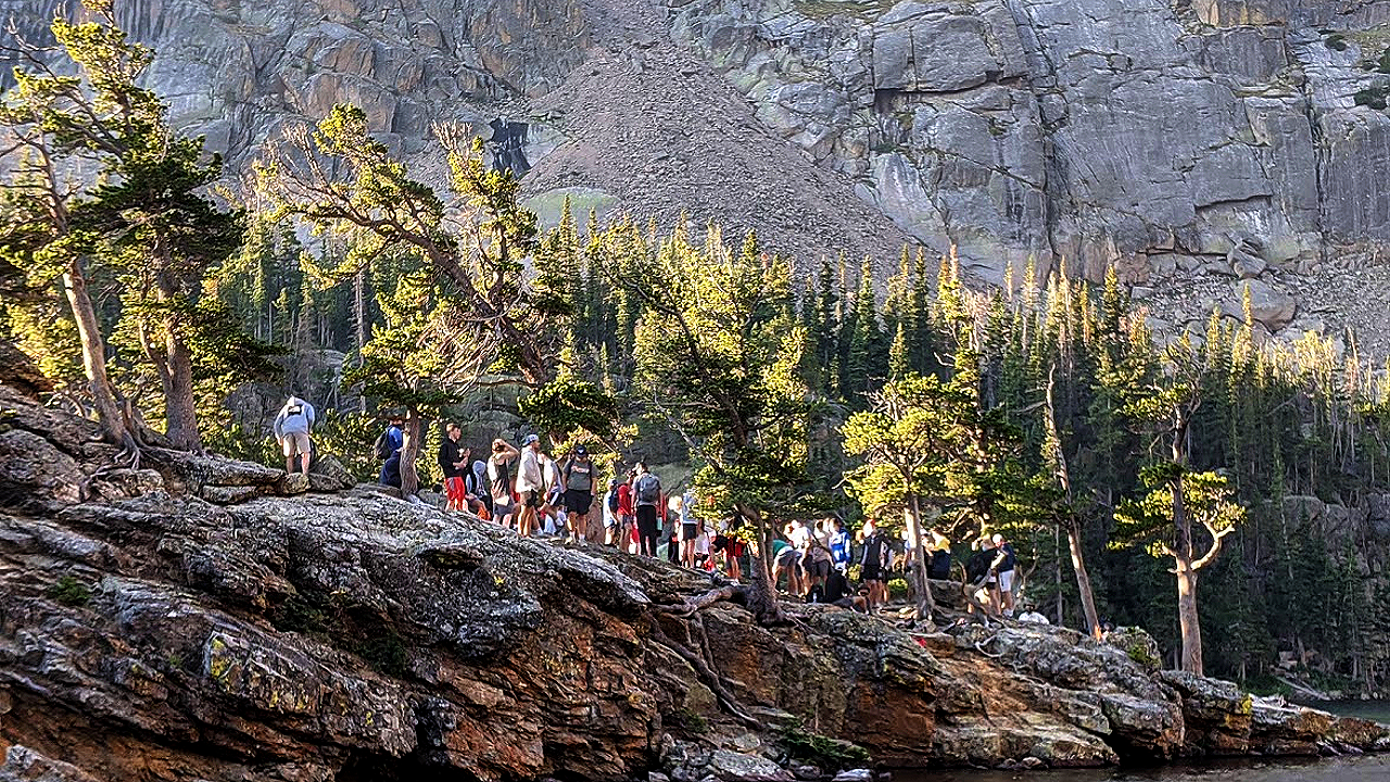 A rocky, tree-filled slope, crowded with hikers