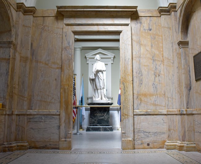 Open door of the Bunker Hill Lodge providing a view into the marble filled lobby and the statuary room with a statue of General Joseph Warren.