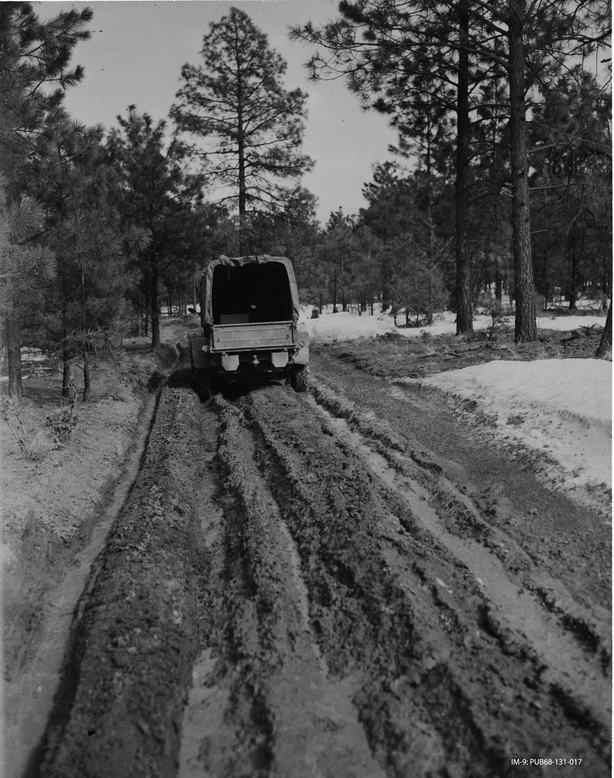 Black and white photo of Army truck in mud, trees surrounding muddy road