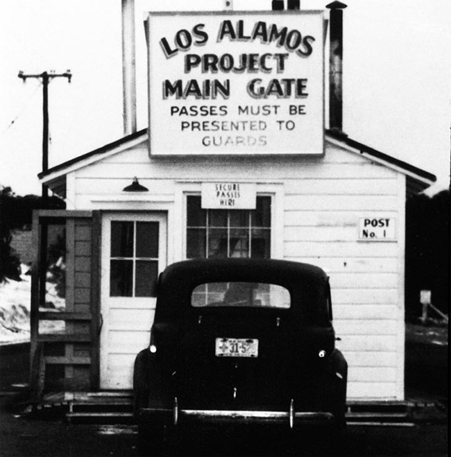 building with car in front, sign reads Los Alamos Project main gate