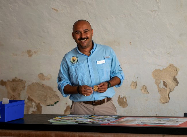 A young man smiles in front of Castillo San Felipe del Morro, with blurred people walking in the background.