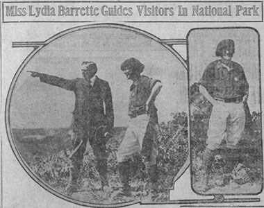 A man points off in the distance to the left as he stands next to a woman wearing breeches with her hands resting on her hips with her elbows pointed out.