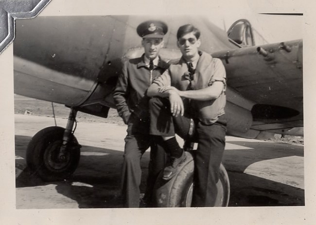 Two men, one in pilot uniform, stand in front of a plane.
