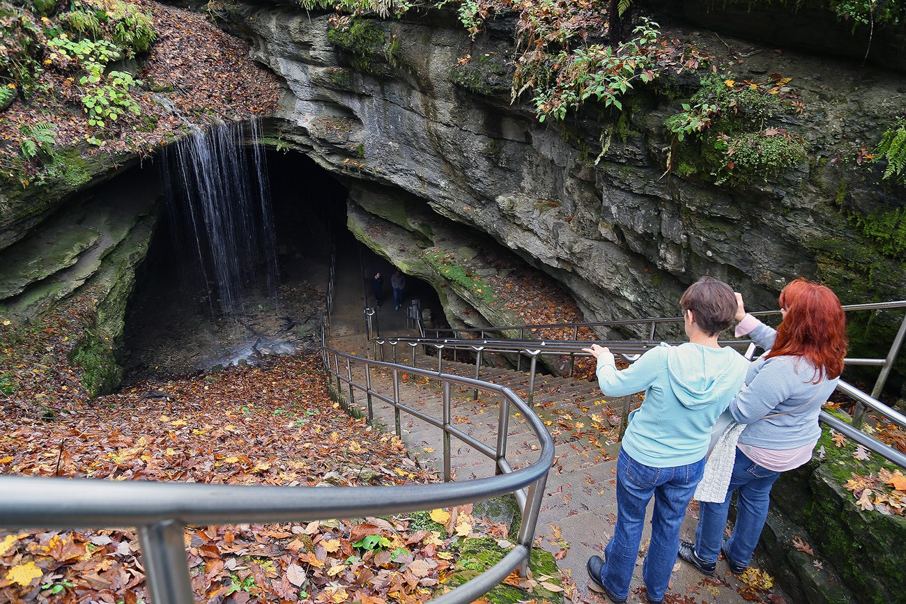 two people look down at the entrance of a cave