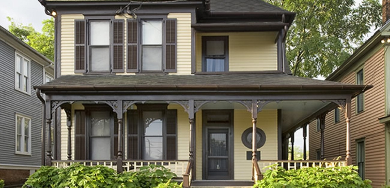 Section of the front of a two-story yellow house with brown trim