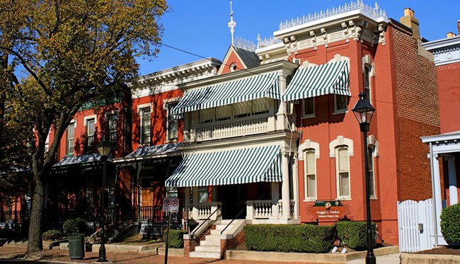 Two-story red brick townhouses with prominent green and white-striped awnings