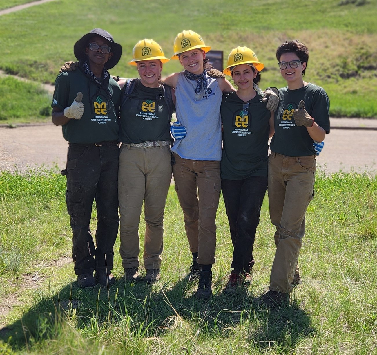 Trail crew members stand next to each other, smiling, posing in hardhats for a photograph.