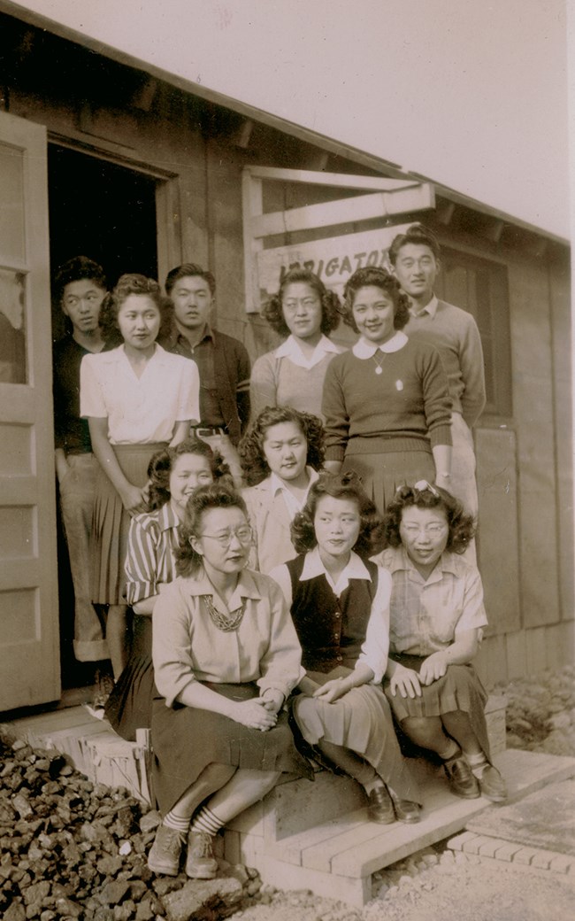 11 Japanese women and 3 men pose for on the front steps of wooden building, sign reads “The Irrigator”