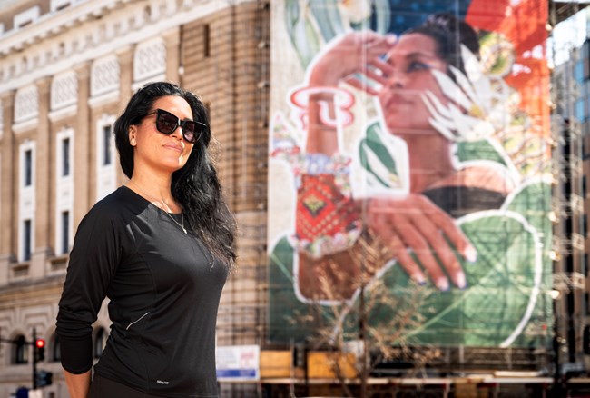 Woman in black shirt and sunglasses standing in front of an art installation on the exterior of the NMWA