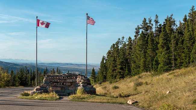 Park sign with Canadian and US flag with mountains in background. Photo by Martin Kraft, CC BY-SA 3.0, https://commons.wikimedia.org/w/index.php?curid=38015817