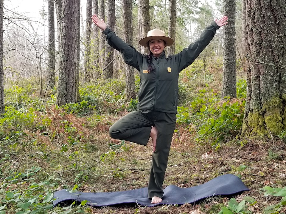 A ranger stands with a yoga pose with arms up balanced on one leg.