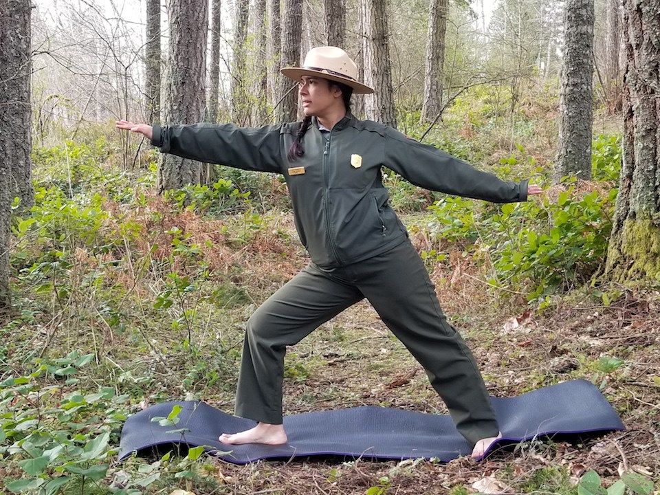 Mount Rainier Yoga: Fisher Warrior Pose A ranger stands in a yoga pose with legs spread in a lunge and arms out to the front and back.