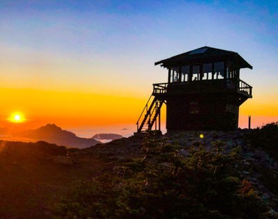 Mt Fremont Lookout at Mount Rainier NP A setting sun turns the sky behind a ridge red-orange and silhouettes a square lookout building.