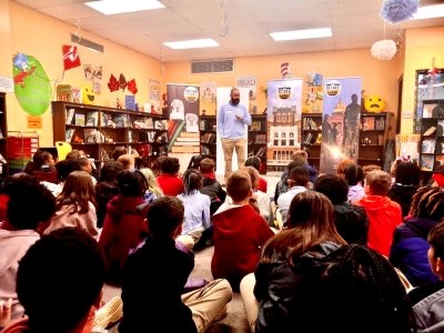 A man presents to a students seated on the floor of a classroom.