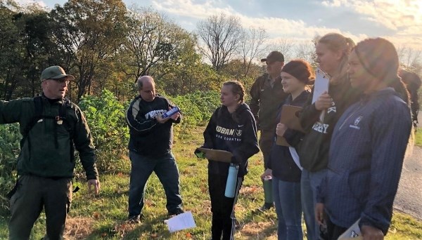 A park ranger speaks to the Archbishop Hoban High School Center for Sustainability members, who are holding clip boards.