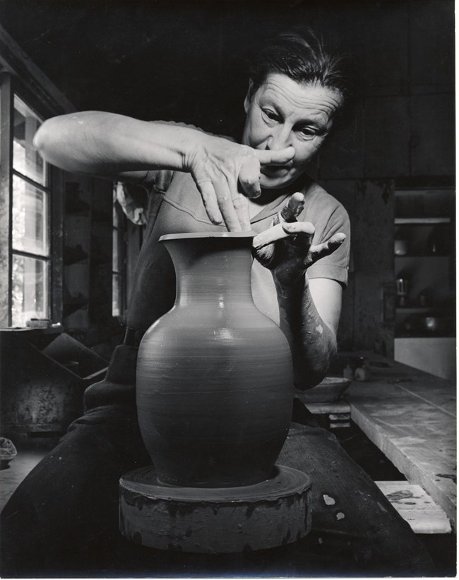 Marguerite ca.1950s Woman concentrates, using tips of fingers to shape the rim of clay vase on potter wheel.