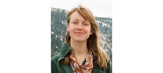 Madeline Duda Duda outside, smiling in front of a tree-and-snow covered landscape.