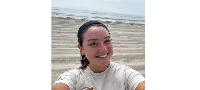 Selfie of smiling woman in white shirt in front of a beach scene
