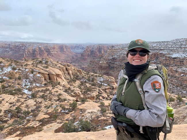 lt= A female park ranger in uniform smiles in front of a canyon.