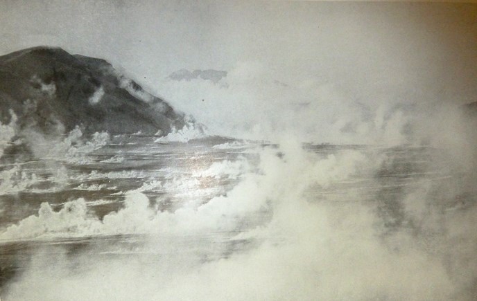 black and white photo of numerous fumaroles steaming in a valley with mountain peak in the distance