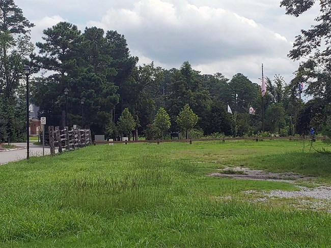 Photo of open landscape and with three flag poles in center and signage across Great Bridge Battlefield Historic Park in the City of Chesapeake, VA.