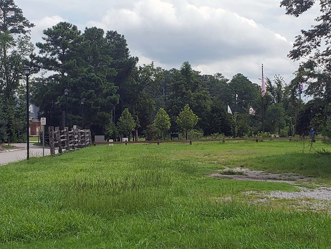 View across the tract to be acquired into the adjacent Great Bridge Battlefield Historic Park in the City of Chesapeake, VA. Photo of open landscape and with three flag poles in center and signage across Great Bridge Battlefield Historic Park in the City of Chesapeake, VA.