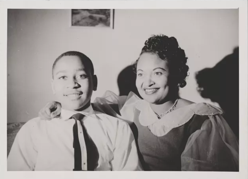 A black and white image of a young boy and his mother smiling for the camera