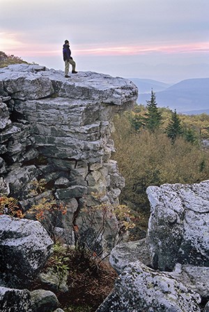 a man standing on the edge of a rocky cliff looking out onto a purple sky