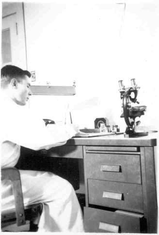 a young man sits at a laboratory desk next to a piece of equipment