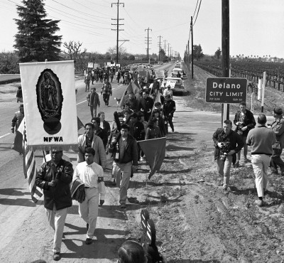 People protesting and marching from Delano to Sacramento. Person in the front is holding a Virgen de Guadalupe image with NFWA letters at the bottom.