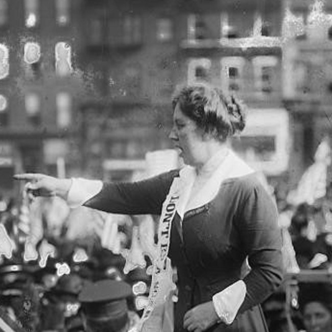 Margaret Hinchey standing and pointing addressing a suffrage rally