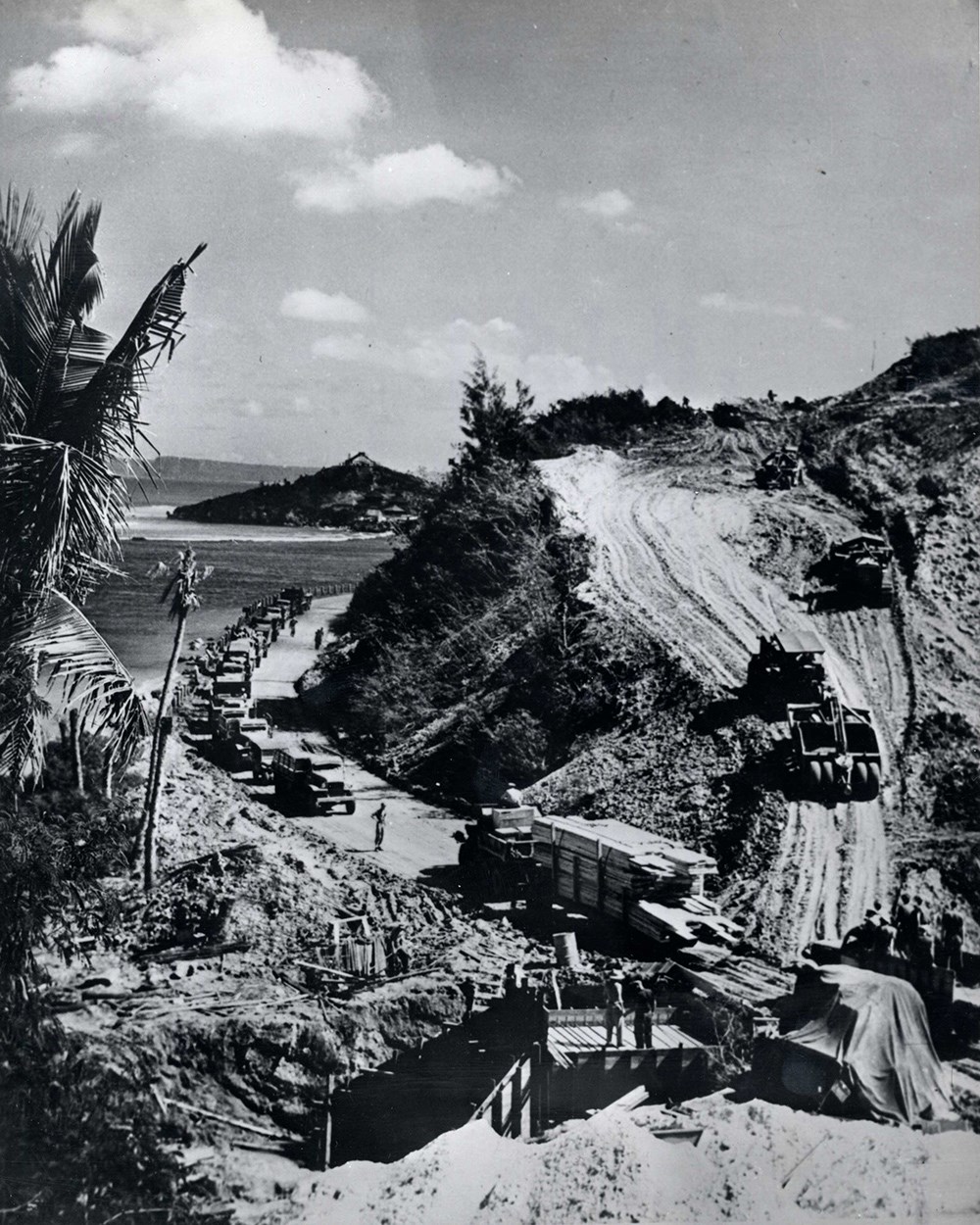Construction crews building a road through a cliff along the edge of the ocean.