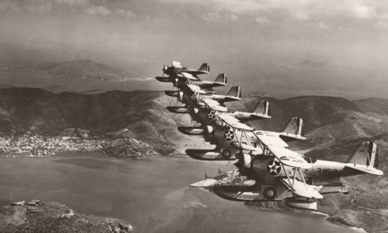 Black and white photo of several World War II airplanes flying over islands and water