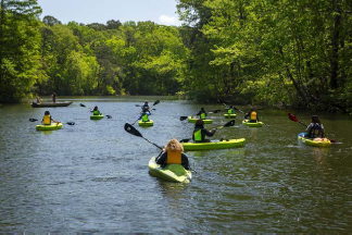 People kayaking on a tree-lined river under a clear sky.