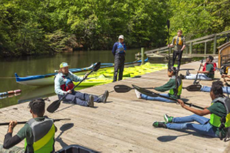 Group of people on a dock holding kayak paddles, with instructors nearby and kayaks by the water.