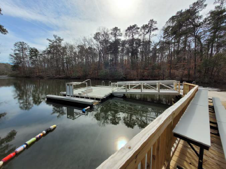 A wooden dock on a lake surrounded by tall trees on a sunny winter day.