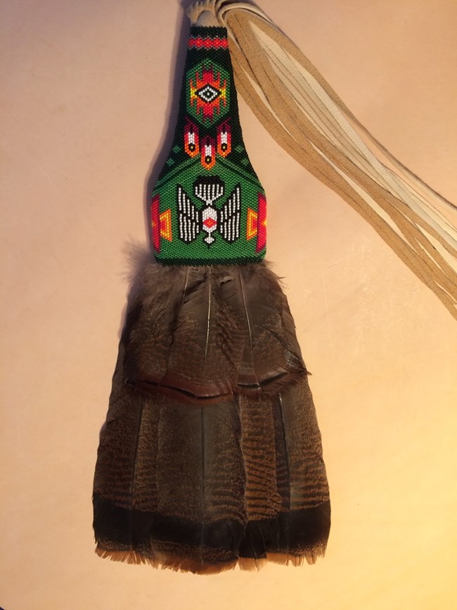 A handheld fan made of turkey feathers and a beaded handle.