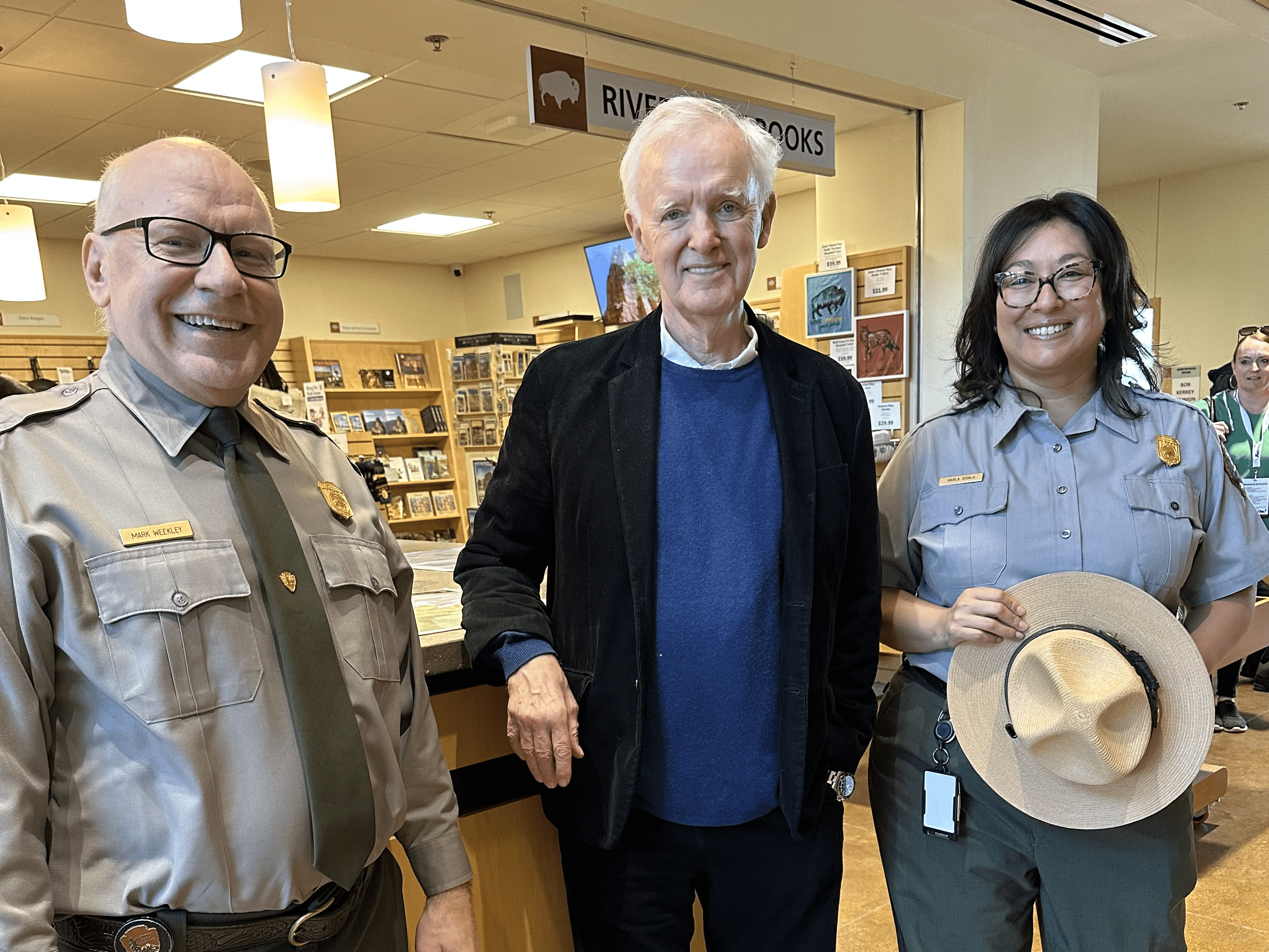 MarkKarlaandbobkerry2 Two people in park ranger uniforms pose with a man in a visitors center