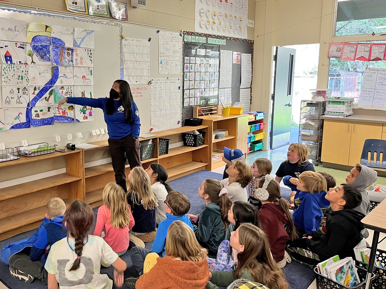 Students review a watershed model Classroom full of students focus their attention towards their instructor as she points to part of a watershed drawing taped up on a whiteboard.