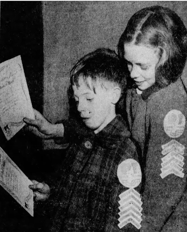Black and white newspaper photo of two white children with Paper Trooper chevrons on their sleeves, holding certificates.