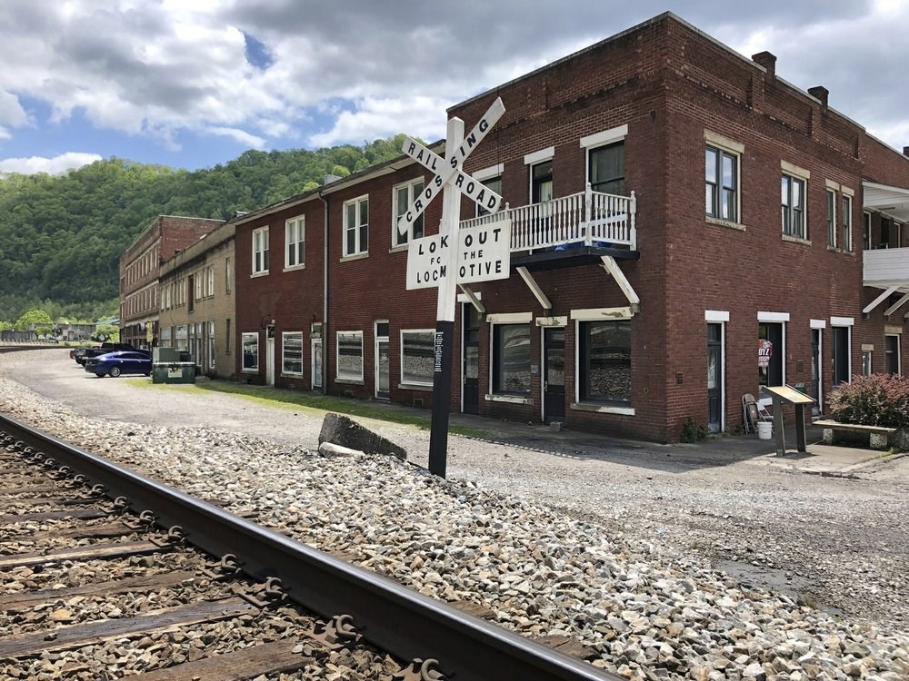 Matewan Historic Disctirc A railway crossing sign stands in front of a row of several brick buildings.