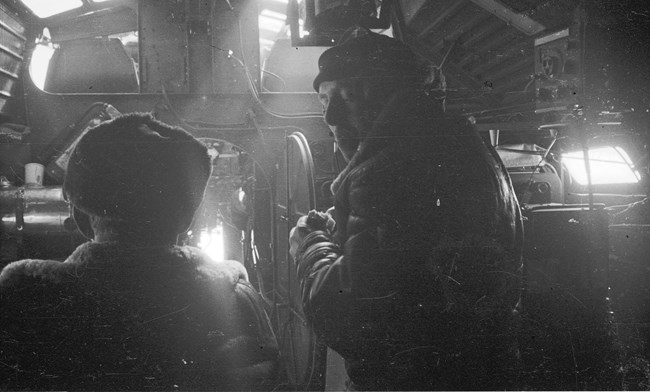 Two men wearing winter clothes inside a plane.