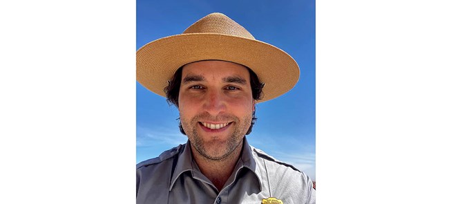 Headshot of smiling man with dark hair, straw hat, and NPS uniform