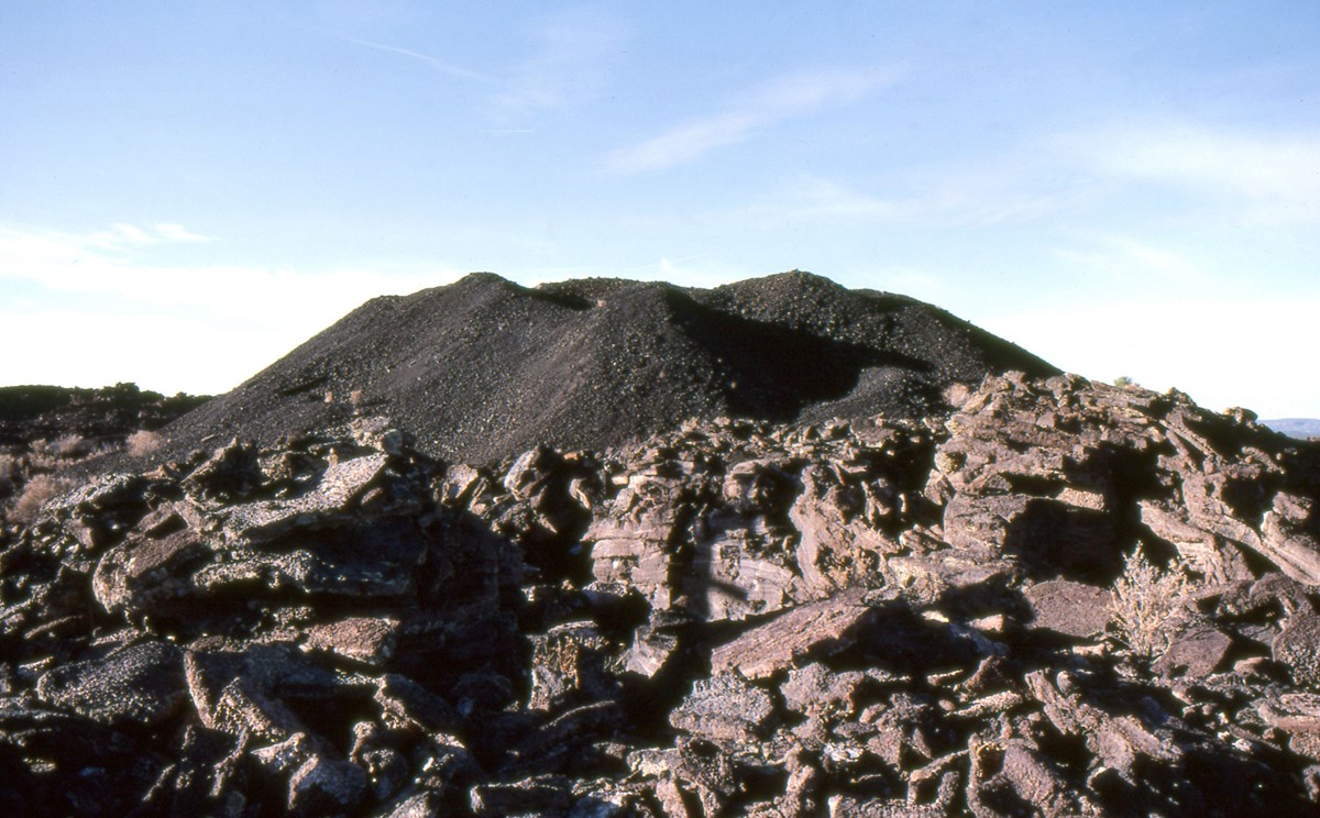a dark cinder cone at the top of a field of broken lava slabs