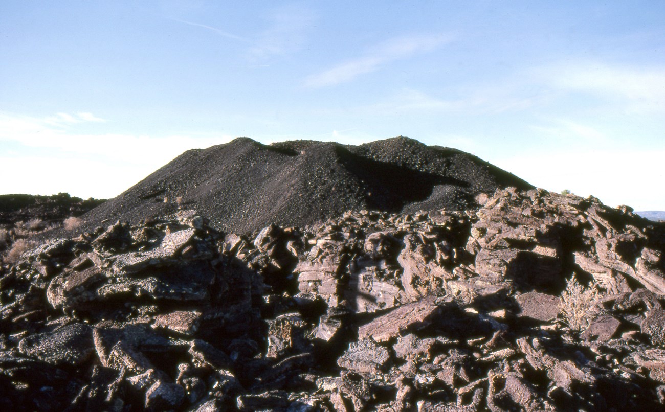 McCartys_vent_1984 a dark cinder cone at the top of a field of broken lava slabs
