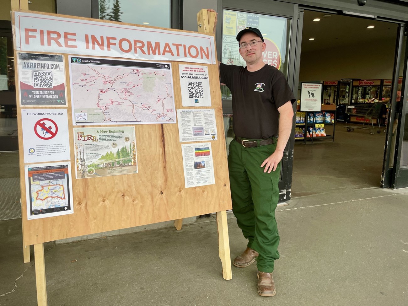 A man stands in front of a large plywood information board containing fire related documents.