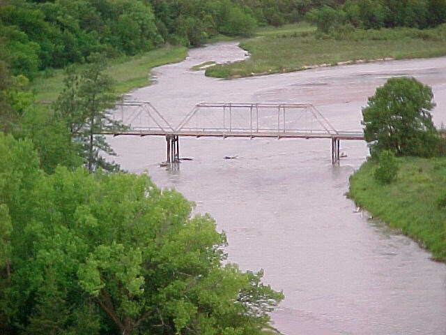 View overlooking a river and bridge, green trees in the foreground.