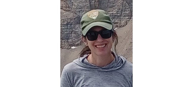 Meg Horner Horner outside in the mountains in a gray shirt and National Park Service ball cap.